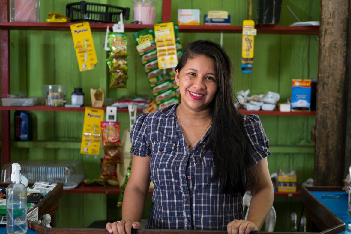 Mulher sorrindo dentro do seu mercado em comunidade no Amazonas.