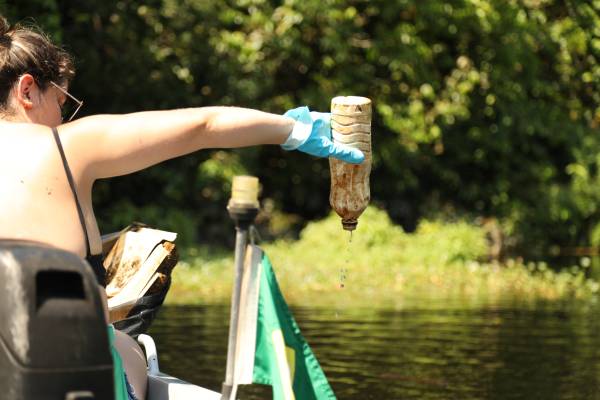 Mulher em barco tirando resíduos sólidos do meio do igarapé em Manaus.