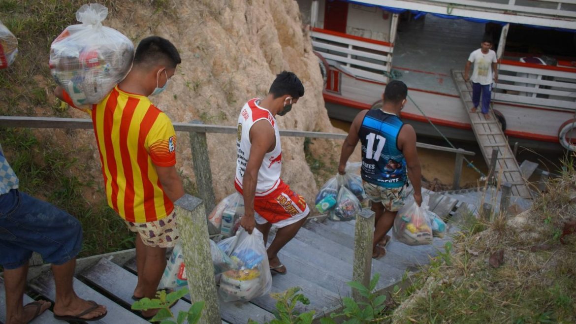 Homens carregando cestas básicas para serem colocadas em barco.