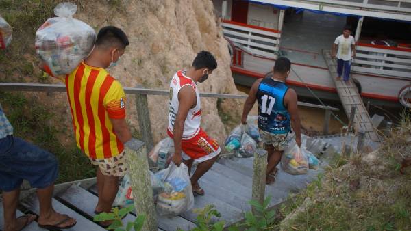 Homens carregando cestas básicas para serem colocadas em barco.