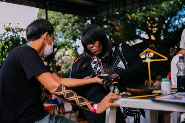 Mulher indígena fazendo pintura em homem durante a Feira da FAS, realizada pela Fundação Amazônia Sustentável (FAS).