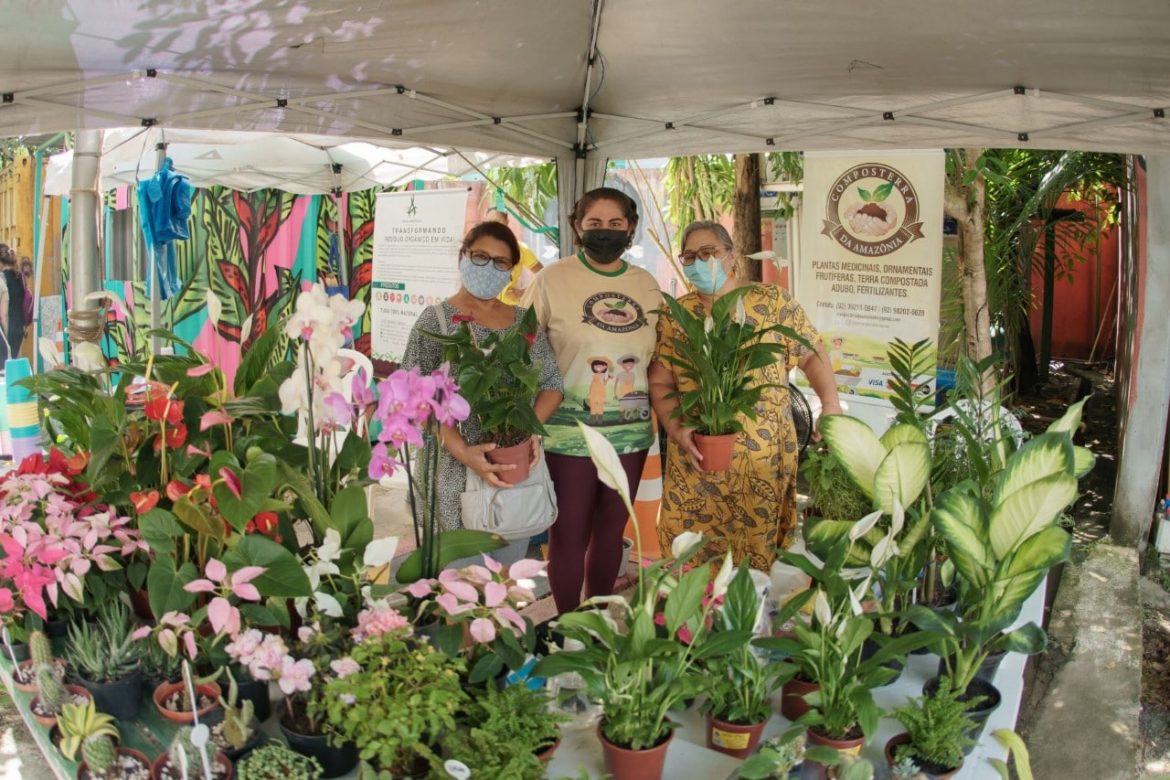 Três mulheres reunidas apresentando vasos com flores na Feira da FAS, realizada pela Fundação Amazônia Sustentável (FAS).