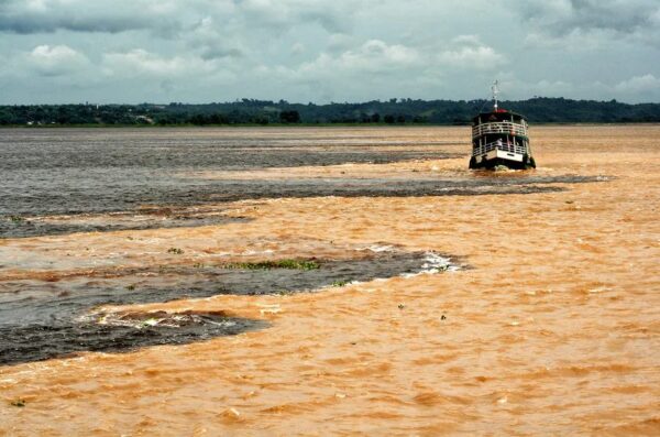 Barco navegando em meio ao encontro das águas, ponto turístico encontrado no Amazonas.